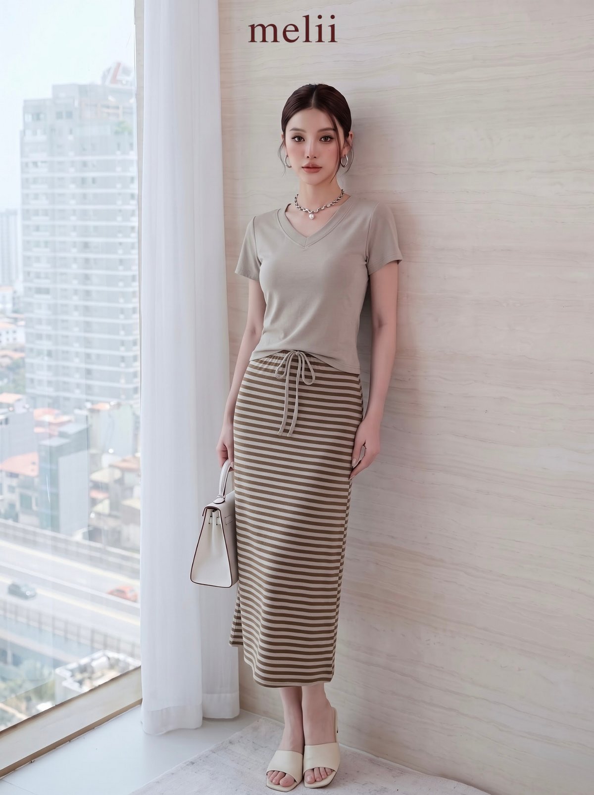 MELII Mira V-Neck Drawstring Top and Striped Maxi Skirt Set in Beige, full-length front model view beside a window