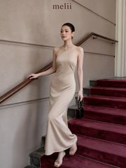 MELII Premium Bodycon Halter Dress in Nude, full-length model view holding the staircase handrail