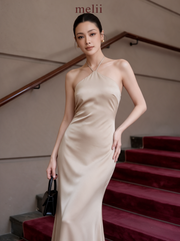 MELII Premium Bodycon Halter Dress in Nude, angled model view with one hand resting at the hip and a black handbag
