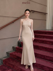 MELII Premium Bodycon Halter Dress in Nude, full-length front model view on a red-carpeted staircase